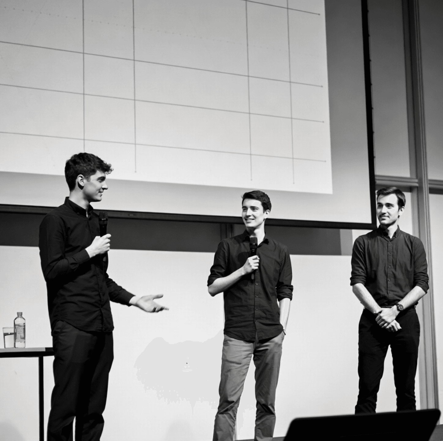 Three engineers presenting on stage at a tech summit, two holding microphones.